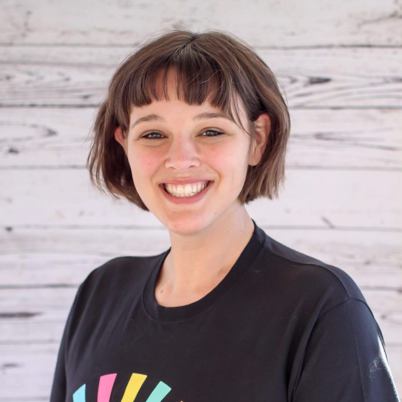 Ann Jonker headshot photo with white wood background, bonnie has light brown hair and a CI Therapies black t-shirt on.