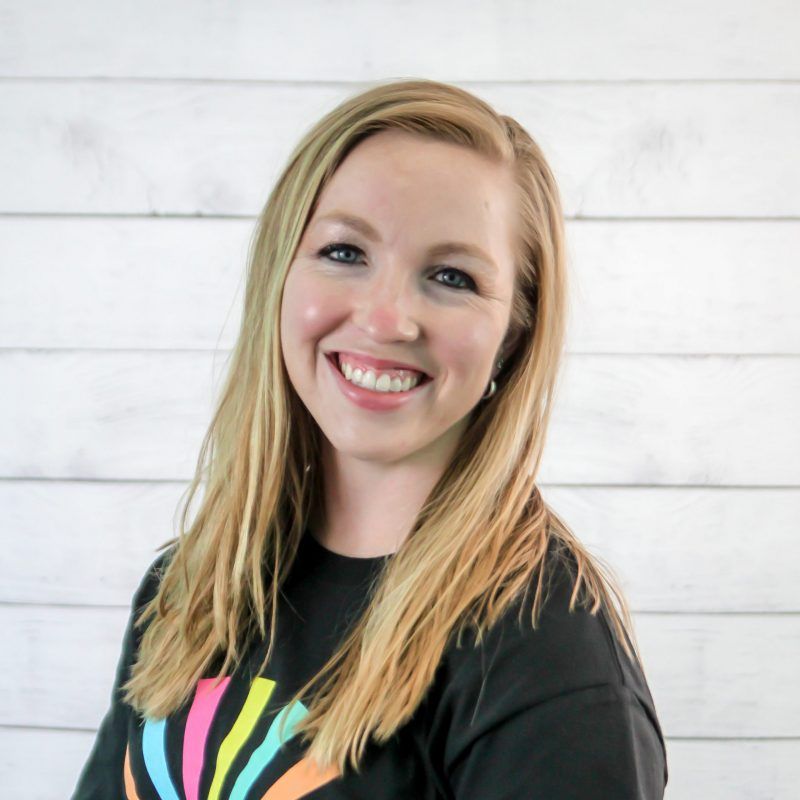 Jen Johnson headshot photo with white wood background, bonnie has light brown hair and a CI Therapies black t-shirt on.
