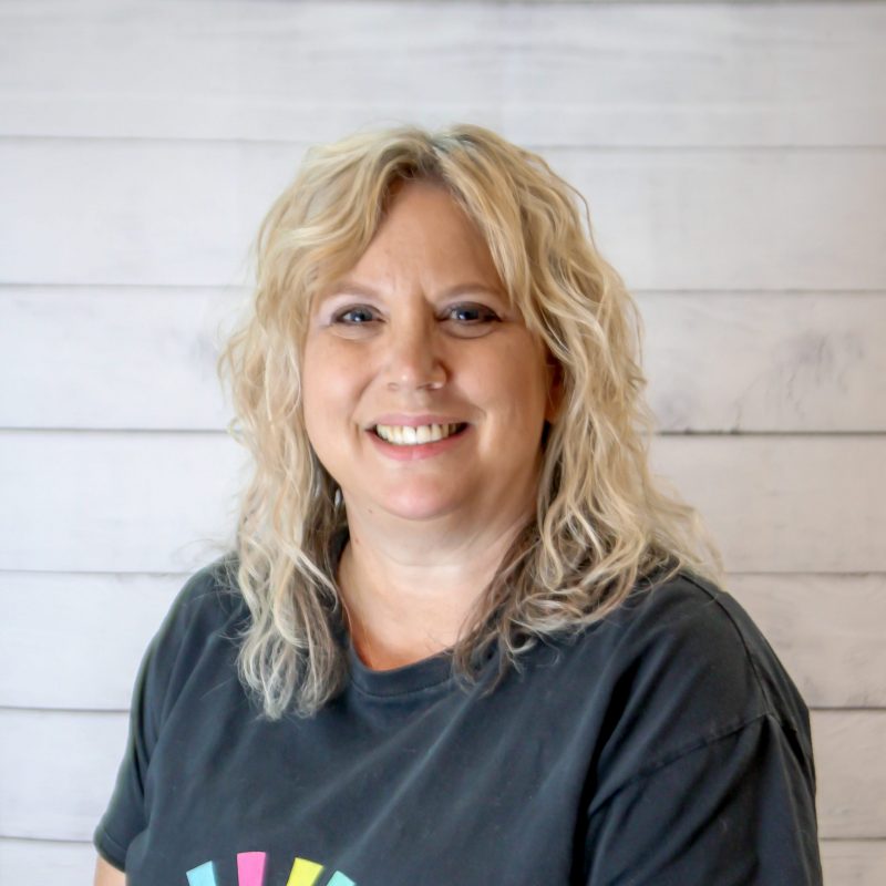 joan a headshot photo with white wood background, bonnie has light brown hair and a CI Therapies black t-shirt on.