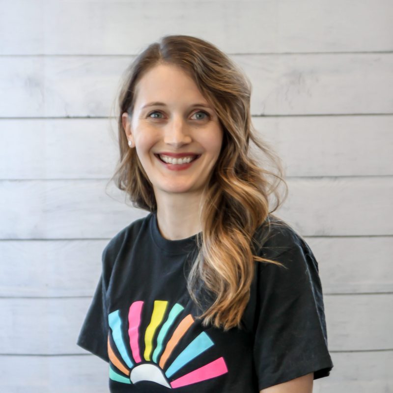 katie brown headshot photo with white wood background, bonnie has light brown hair and a CI Therapies black t-shirt on.