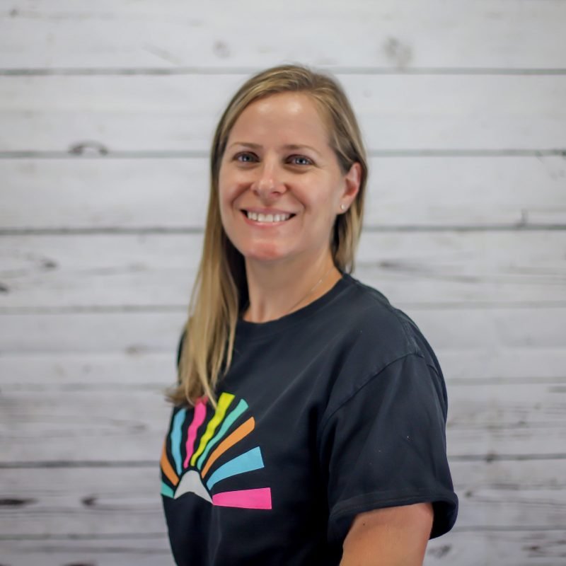 michelle hollman headshot photo with white wood background, bonnie has light brown hair and a CI Therapies black t-shirt on.