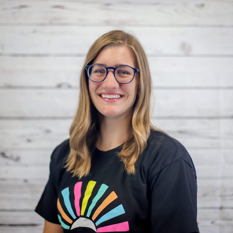 taylor wienkes headshot photo with white wood background, bonnie has light brown hair and a CI Therapies black t-shirt on.